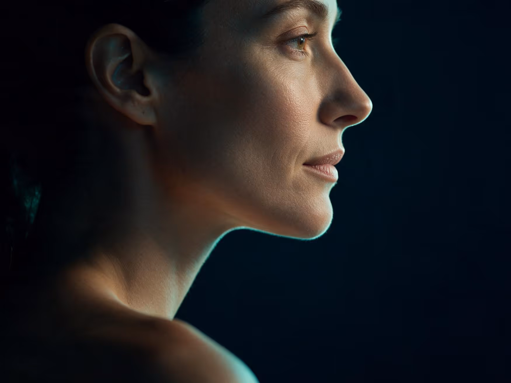 Perfil de uma mulher em luz baixa, com o contorno do maxilar, do mento e do nariz desenhado pela luz